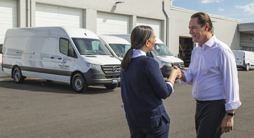 a man and woman shaking hands in front of white vans