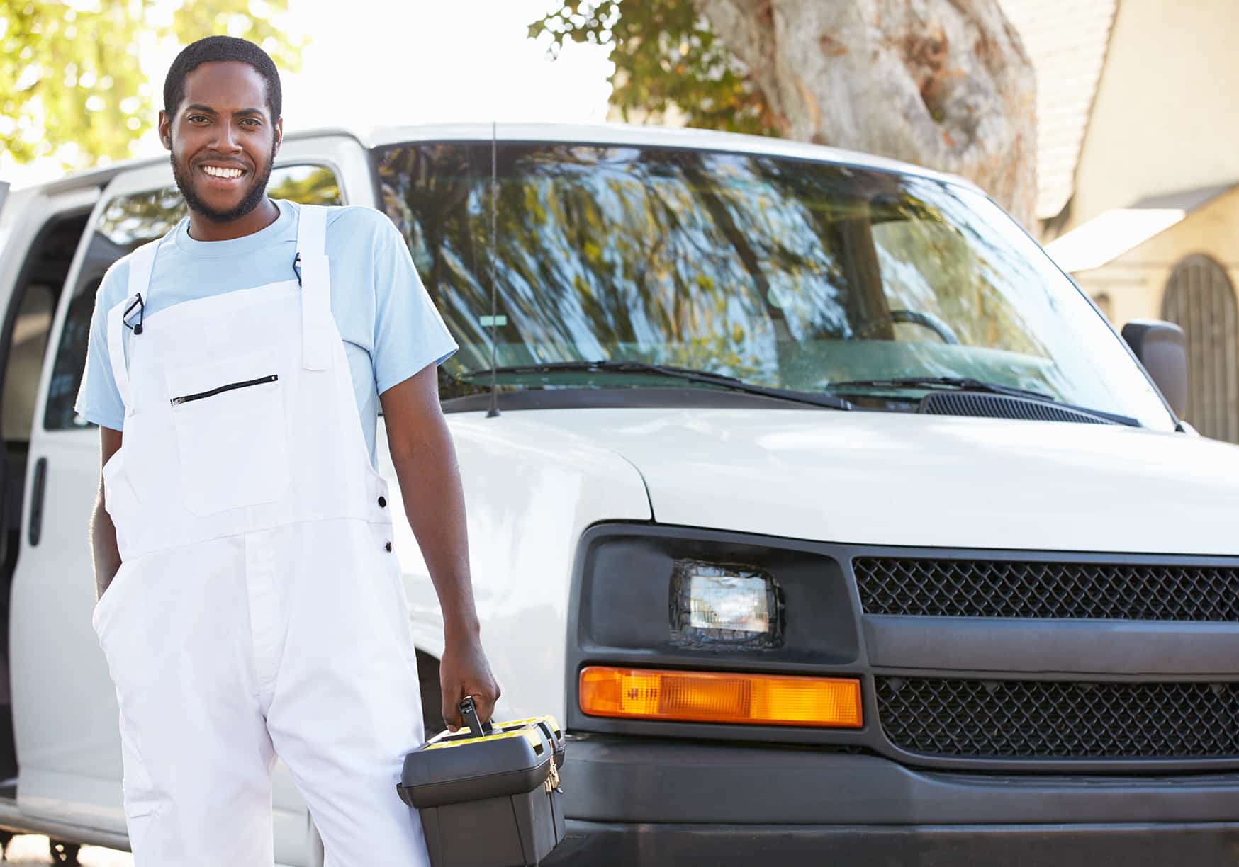 a man in white overalls holding a toolbox next to a white van