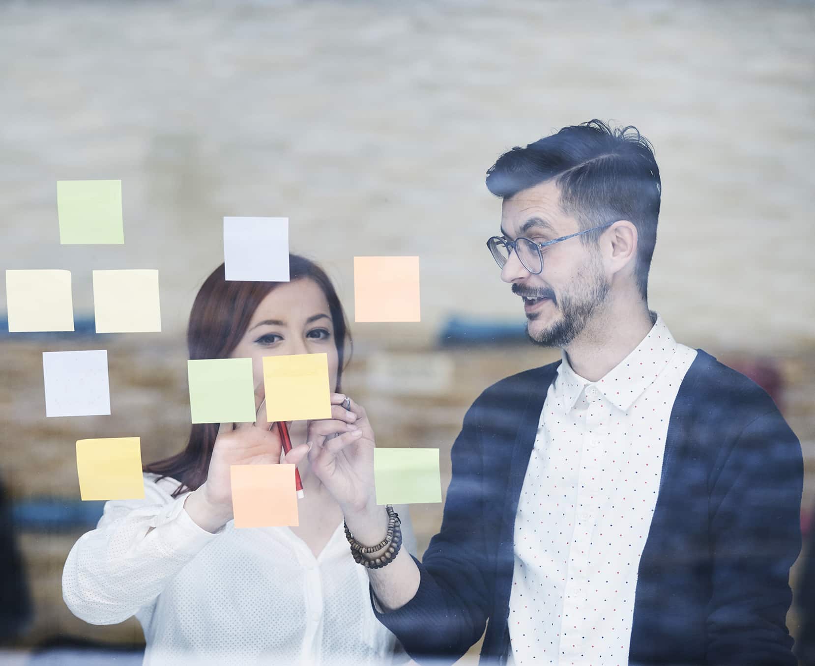 a man and woman looking at sticky notes on a glass wall