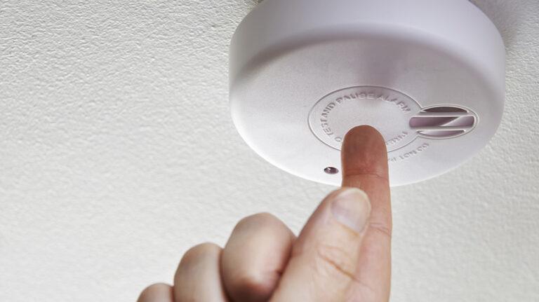 a finger pressing a button on a smoke detector